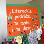 Powiększ zdjęcie Na zdjęciu pomarańczowa tablica z białym na napisem literackie podróże te małe i te duże oraz skarpetki przypięte spinaczami do sznurka w oddziale dla dzieci w bibliotece