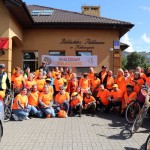 Powiększ zdjęcie Grupowe zdjęcie rowerzystów w pomarańczowych koszulkach na tle biblioteki