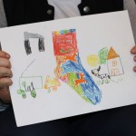 Powiększ zdjęcie Na zdjęciu praca plastyczna przedstawiająca skarpetkę maszyny rolnicze krowę i dom narysowane kredkami