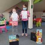 Powiększ zdjęcie W Bibliotece Hania i Zuzia laureatki konkursu trzymające dyplomy obok stoją torby z nagrodami 