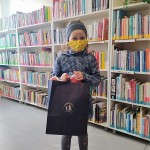 Powiększ zdjęcie W Bibliotece Lena laureatka konkursu trzymająca dyplom obok stoi torba z nagrodą 