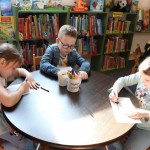 Powiększ zdjęcie Dzieci siedzą przy stoliku i kolorują dinozaura