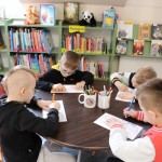Powiększ zdjęcie Chłopcy siedzą przy stoliku i kolorują dinozaura