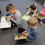 Powiększ zdjęcie Dzieci siedzą na podłodze w bibliotece i oglądają książki o dinozaurach
