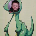 Powiększ zdjęcie Chłopiec w fotobudce zielonego dinozaura