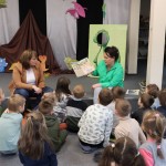 Powiększ zdjęcie Dzieci siedzą na podłodze w bibliotece słuchają pani czytającej bajkę